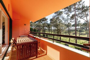 Varanda com mesa e cadeiras de madeira, corrimão e vista para área arborizada.