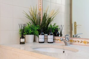 Casa de banho com lavatório, duas plantas em vasos e duas embalagens de sabonete líquido para as mãos.