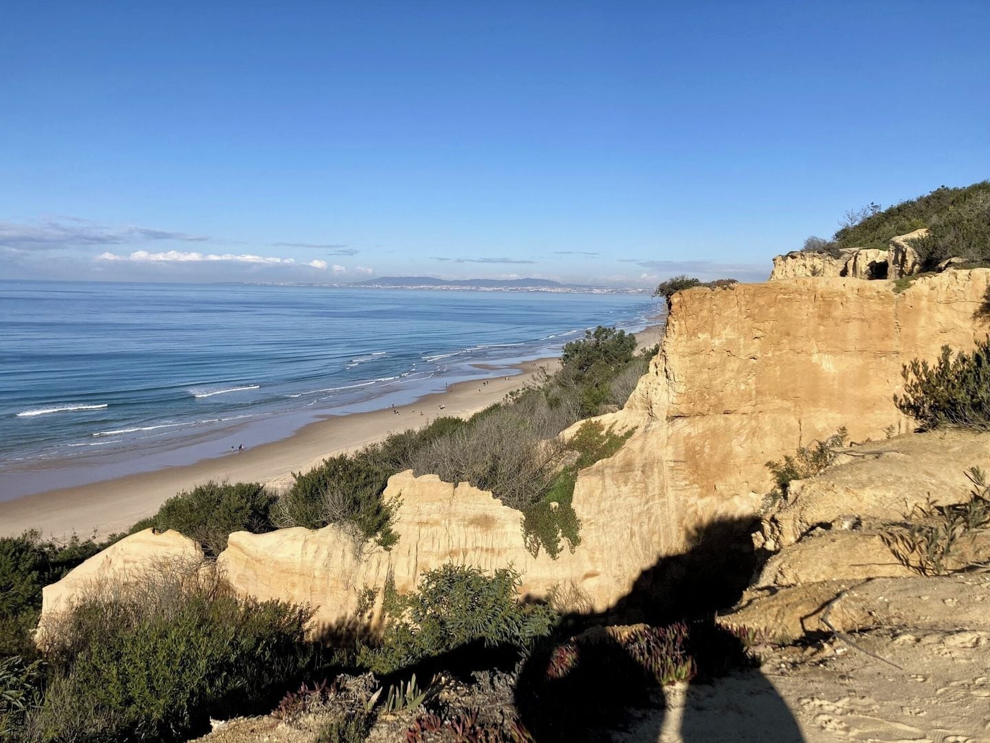A coastal landscape with a cliff overlooking a beach and the ocean.