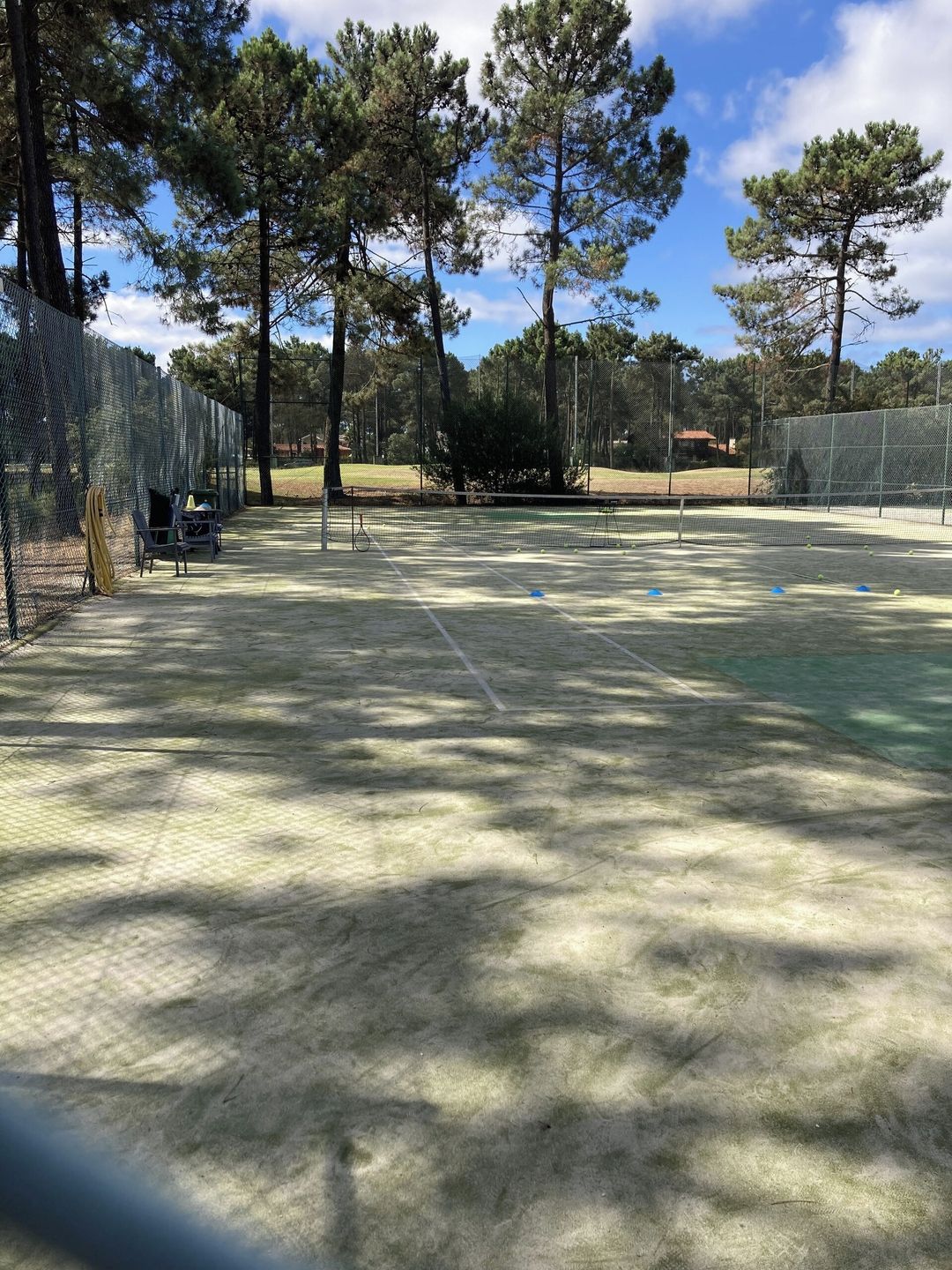 An outdoor tennis court with a net, surrounded by trees and a fence.