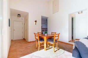 A dining area with a wooden table and chairs, a small potted plant, and a white door leading to a kitchen.