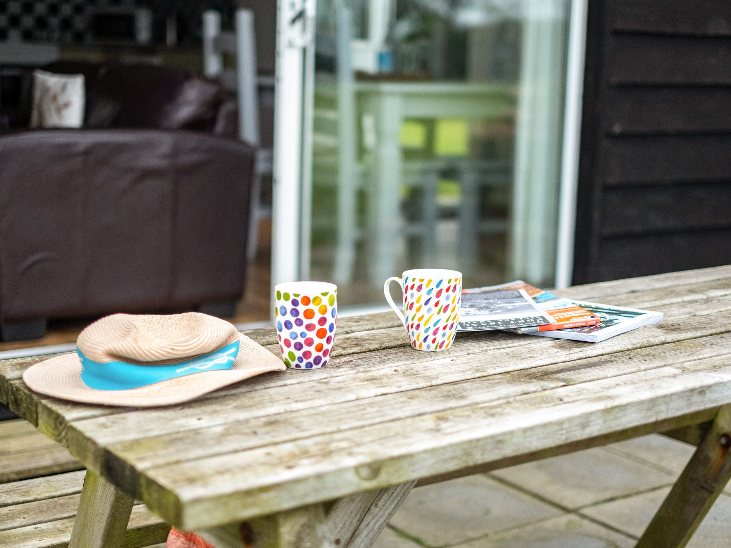 A wooden table with a hat, a polka-dotted mug, and a magazine.