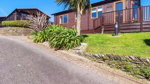 A row of wooden cabins with a stone wall and greenery in front. - Chi Prenn Byhan (Tintagel)