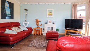 A living room with a red sofa, a television, a fireplace, and a painting on the wall. - Chi Prenn Byhan (Tintagel)