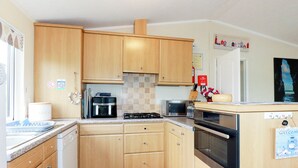 A compact kitchen with wooden cabinets, a gas stove, a microwave, and a refrigerator. - Chi Prenn Byhan (Tintagel)