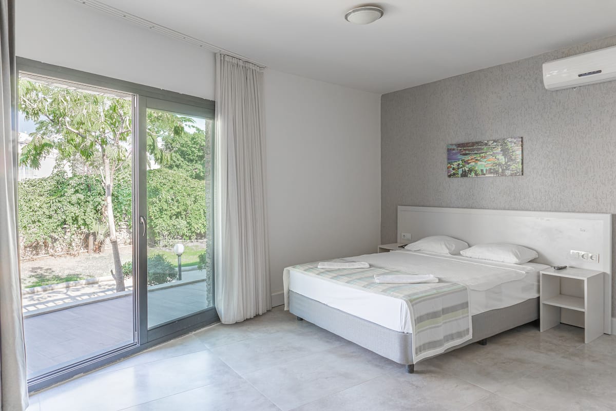 Un dormitorio moderno con una cama grande, una mesita de noche y vistas al exterior a través de un ventanal corredera.