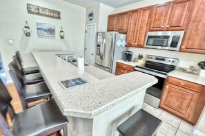 A kitchen with granite countertops, wooden cabinets, stainless steel appliances, and a bar area with stools.