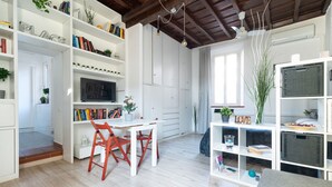 Una sala de estar moderna con muebles blancos, un comedor y una estantería llena de libros y objetos decorativos.