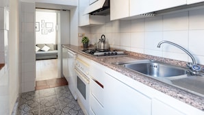 Una cocina compacta con gabinetes blancos, un lavamanos de acero inoxidable, una estufa a gas y un piso de baldosas con diseño.
