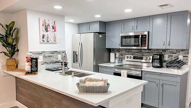 A modern kitchen with grey cabinets, stainless steel appliances, a central island, and a potted plant. - Fabulous Apartment near Disney (Kissimmee)