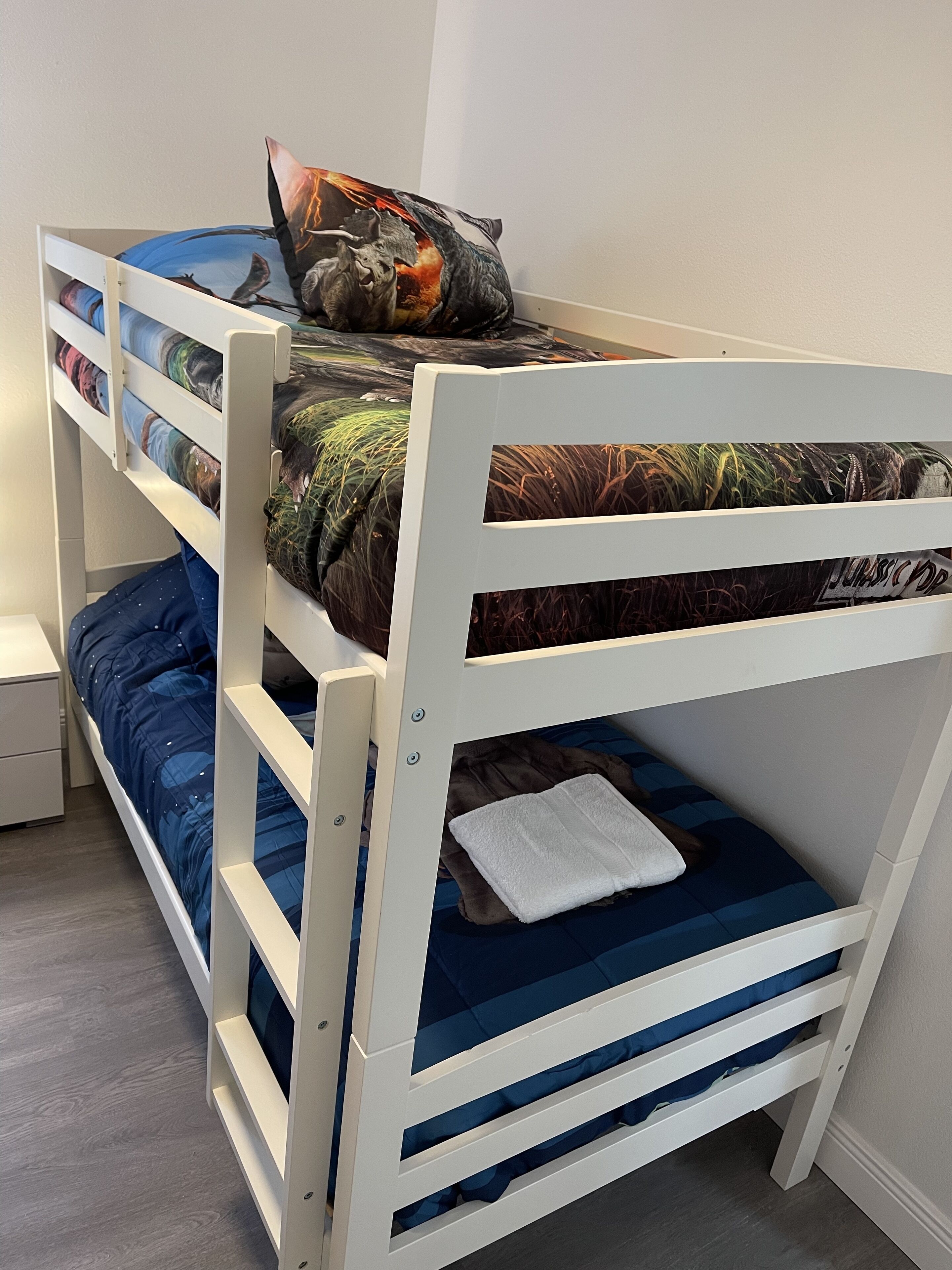 A bunk bed with a dinosaur-themed pillow and a white towel on the lower bunk.