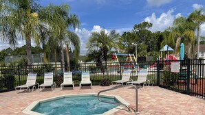A swimming pool with lounge chairs, a fenced playground area, and palm trees. - Fabulous Apartment near Disney (Kissimmee)