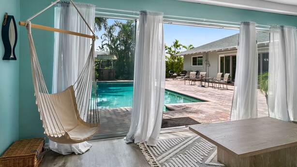 Una habitación con una silla hamaca, una piscina y un patio con mobiliario exterior.