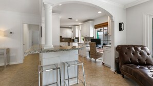 Una cocina amplia con armarios blancos, encimera de granito y una isla central con taburetes de bar.
