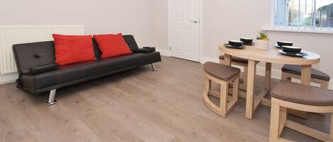 A modern living space with a black sofa, red cushions, a wooden dining table, and matching stools.