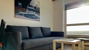 Un salon moderne avec un canapé gris, une petite table basse en bois et une grande fenêtre donnant sur une zone boisée.