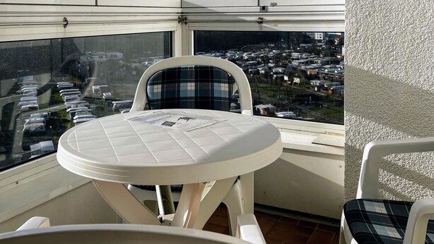 Un balcon avec une table et des chaises, une vue sur un parking et un ciel dégagé.