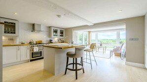 Une cuisine moderne avec des meubles blancs, un îlot central et une vue sur l’extérieur.