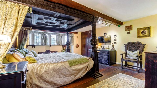 Une chambre à coucher de style traditionnel, avec un lit à baldaquin, une chaise en bois, une télévision et un bureau avec une lampe.