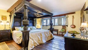 Un lit à baldaquin en bois, un bureau en bois avec une lampe et une fenêtre avec des rideaux.