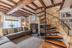 A cozy living room with a stone fireplace, a wooden staircase, and a bookshelf.