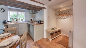 Een keuken met houten balken, een raam en een eethoek met een gedekte tafel voor twee personen.