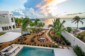 A modern pool area with a view of the sea, surrounded by tropical plants and a white building. - SulMare at Sapodilla Bay Luxury villas (Providenciales)