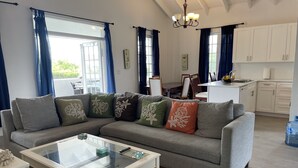 Ein modernes Wohnzimmer mit einer Eckcouch, einem Glastisch und einem Essbereich im Hintergrund.