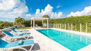 Ein rechteckiger Pool mit einer weißen Pergola und Liegestühlen mit blauen Kissen.