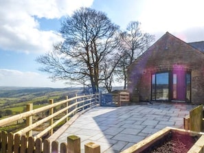 A stone building with a large window and a wooden fence overlooking a valley. - The Barn at Hill House (Buxton)