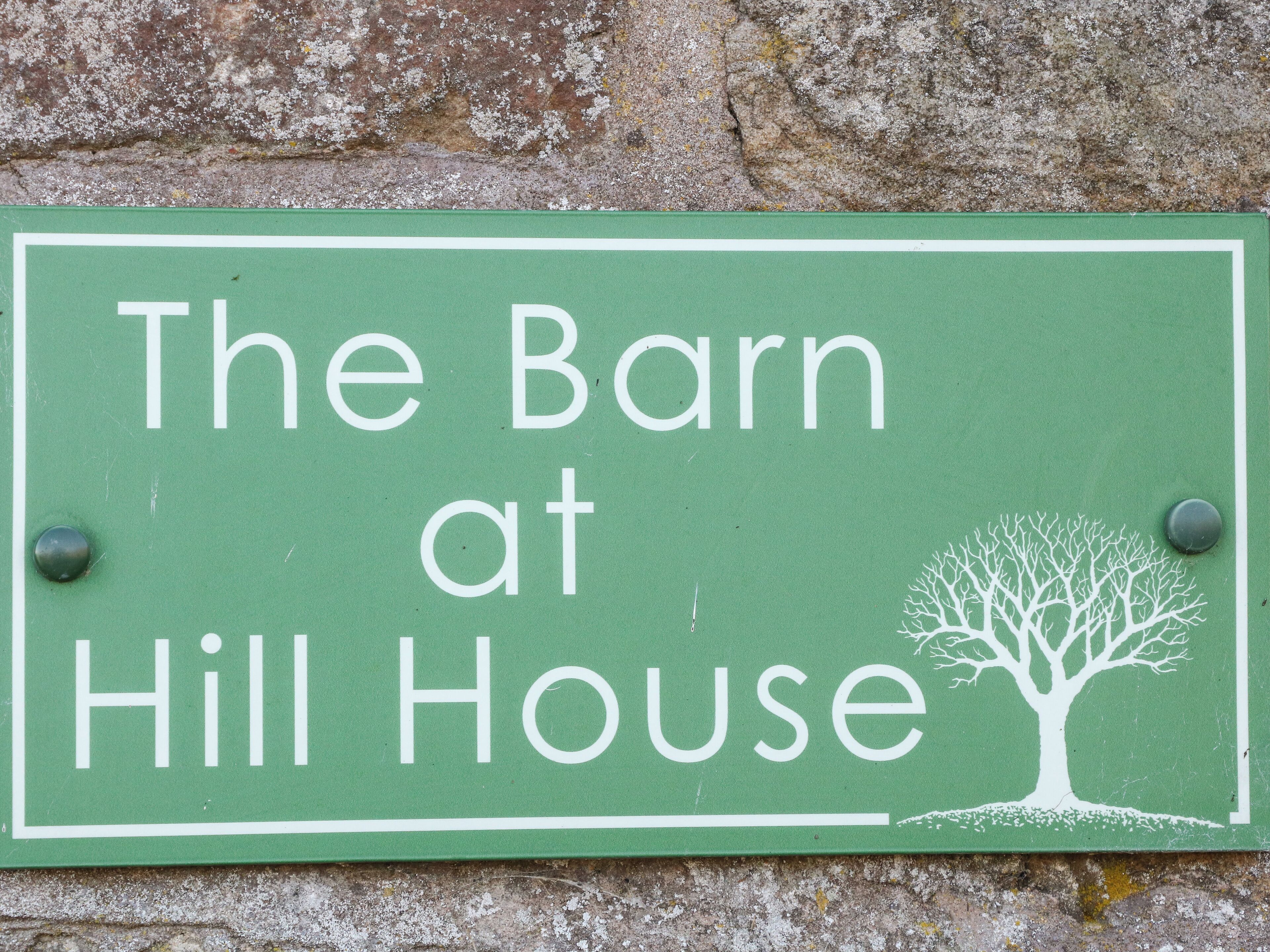 A green sign with white lettering that reads "The Barn at Hill House."