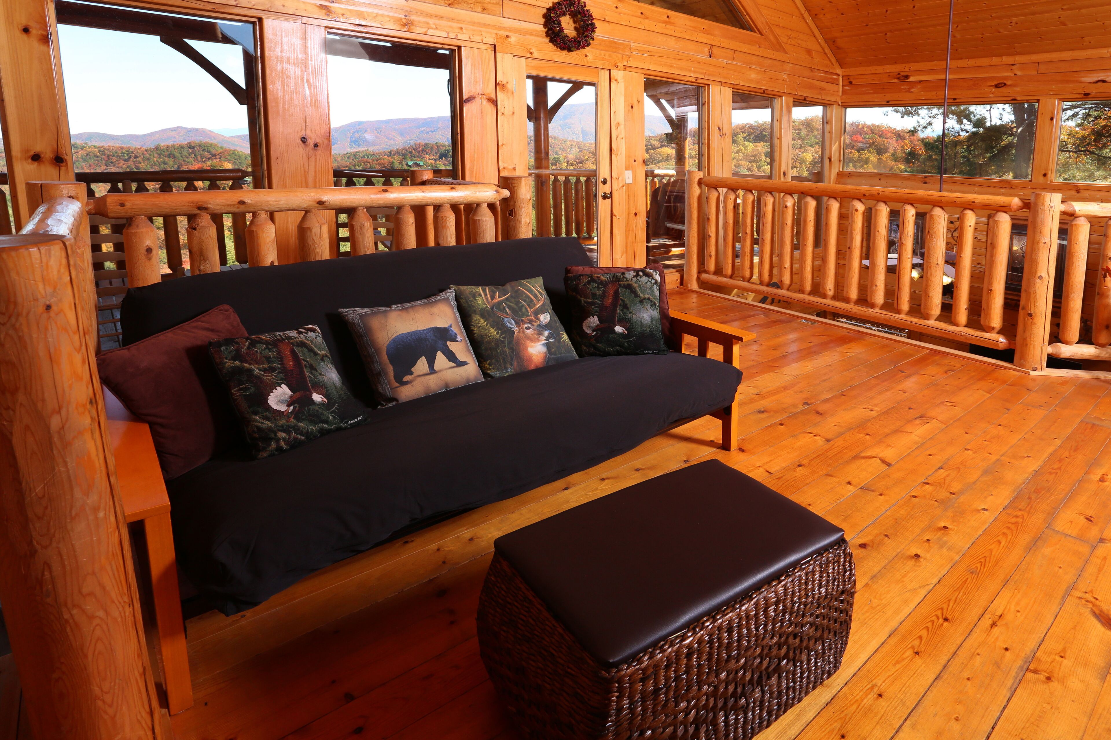 A wooden cabin with a sofa and ottoman, large windows, and a view of mountains.
