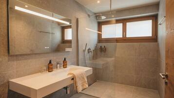 Un baño moderno con ducha de vidrio, tocador con espejo y ventana sobre el lavabo.