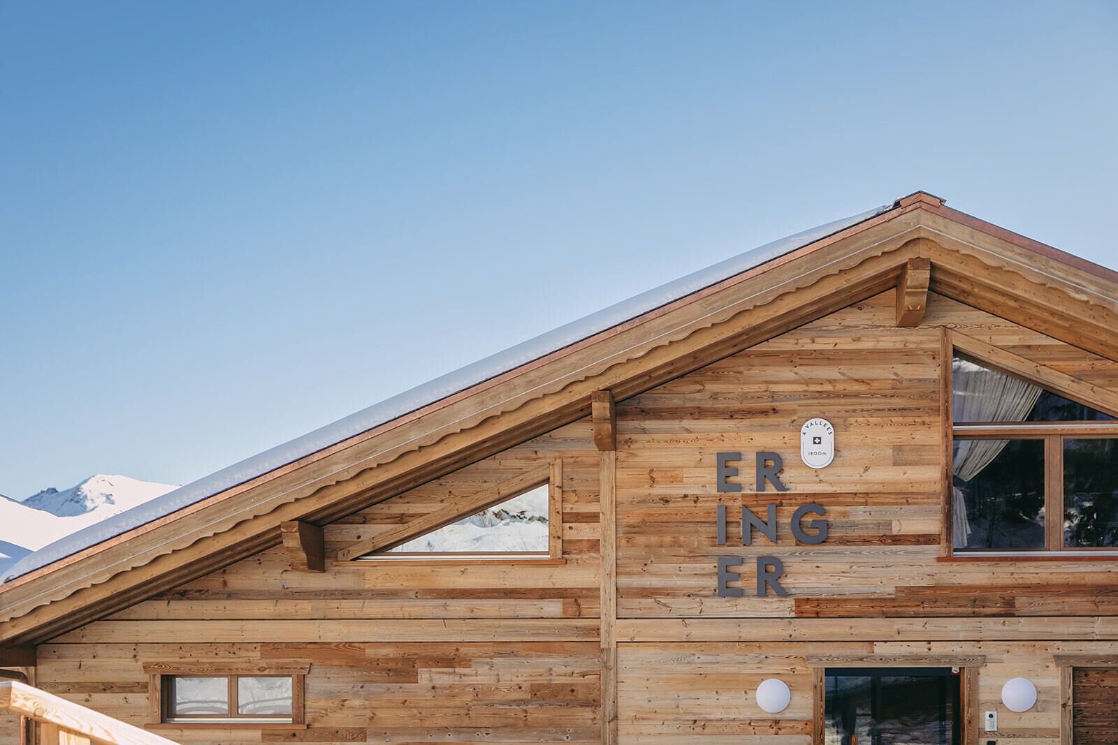A wooden mountain cabin with a sloped roof, large windows, and a sign reading "ERINGER."