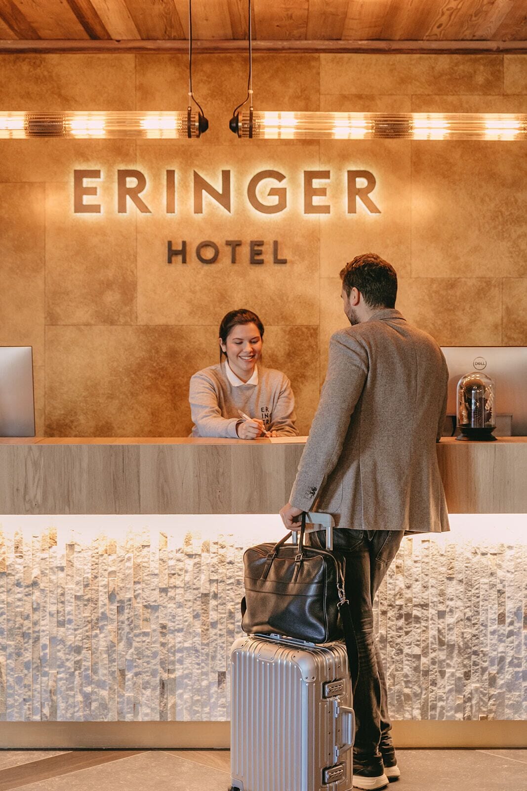 A reception desk at the Eringer Hotel with a receptionist and a guest standing in front of it.