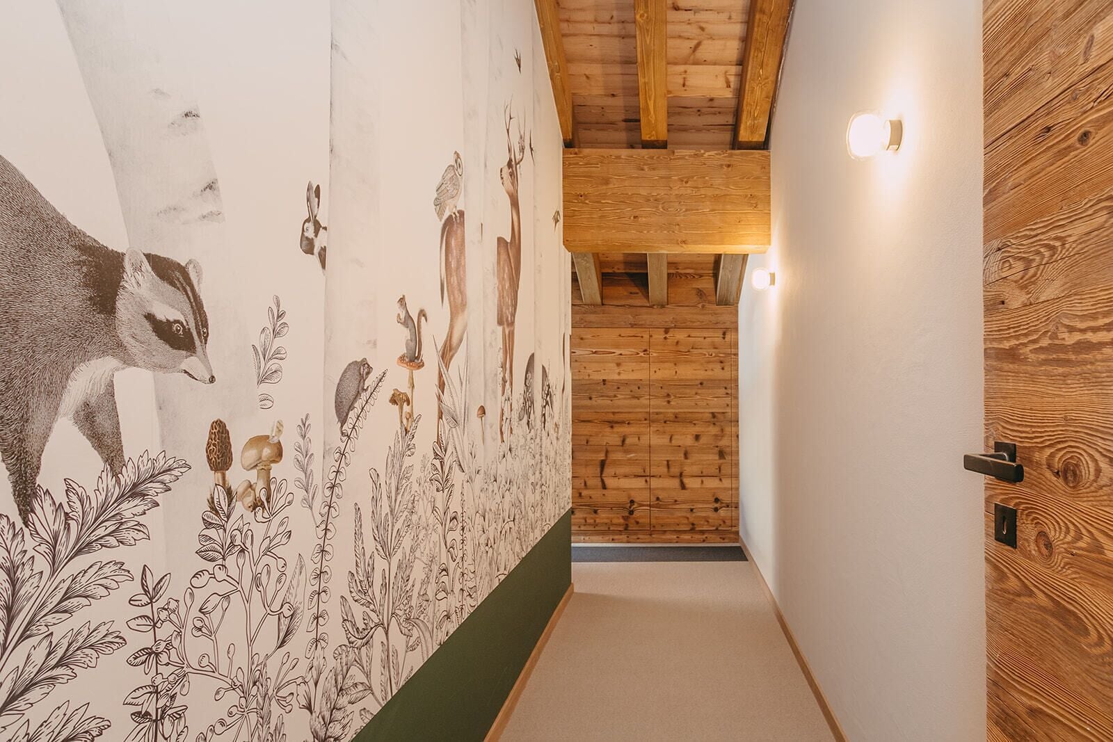 Um corredor estreito com uma porta de madeira à direita e um mural à esquerda retratando animais e plantas.
