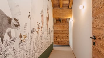 Um corredor estreito com uma porta de madeira à direita e um mural à esquerda retratando animais e plantas.