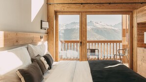 A bedroom with a large bed, a wooden headboard, and a balcony with a mountain view. - Eringer Hotel (Heremence)