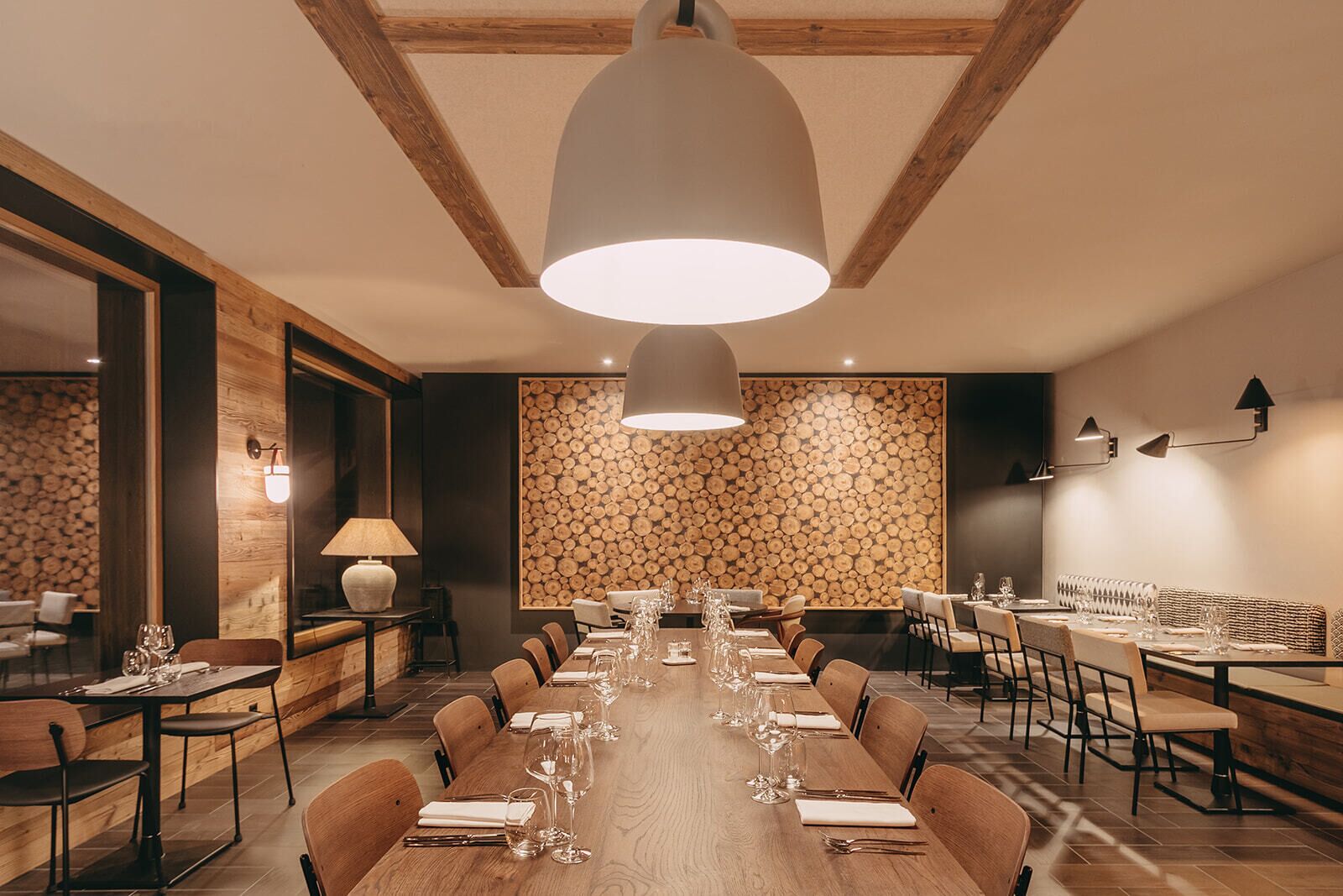 A dining area with a long wooden table set for a meal, surrounded by chairs, with a large pendant light above.