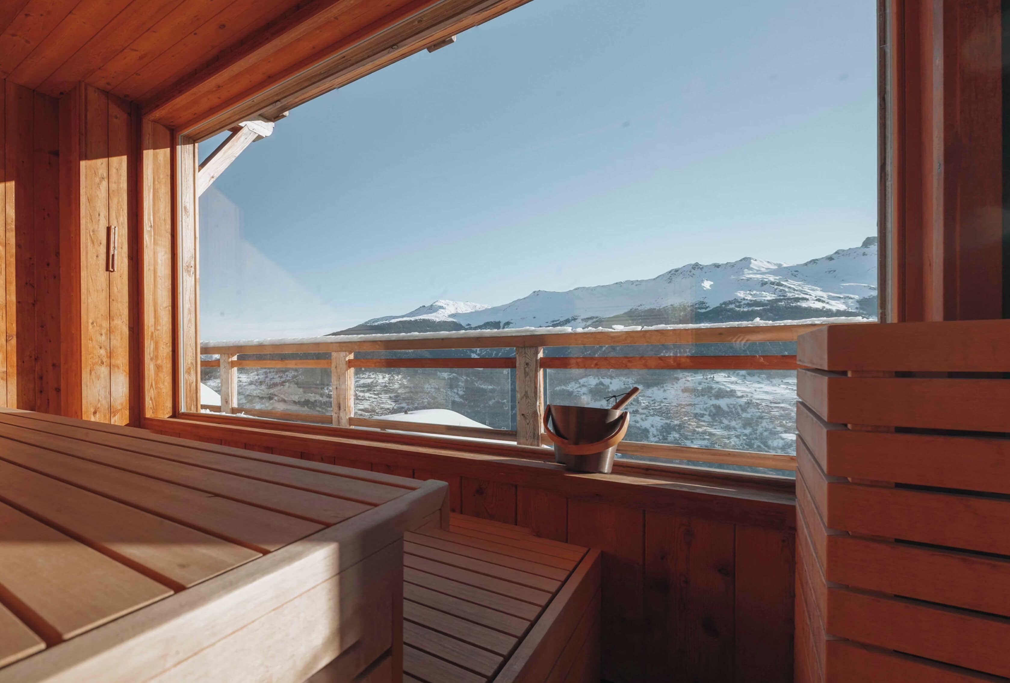 Eine Holzhütte mit einer Bank und einem Fenster mit Blick auf einen verschneiten Berg.