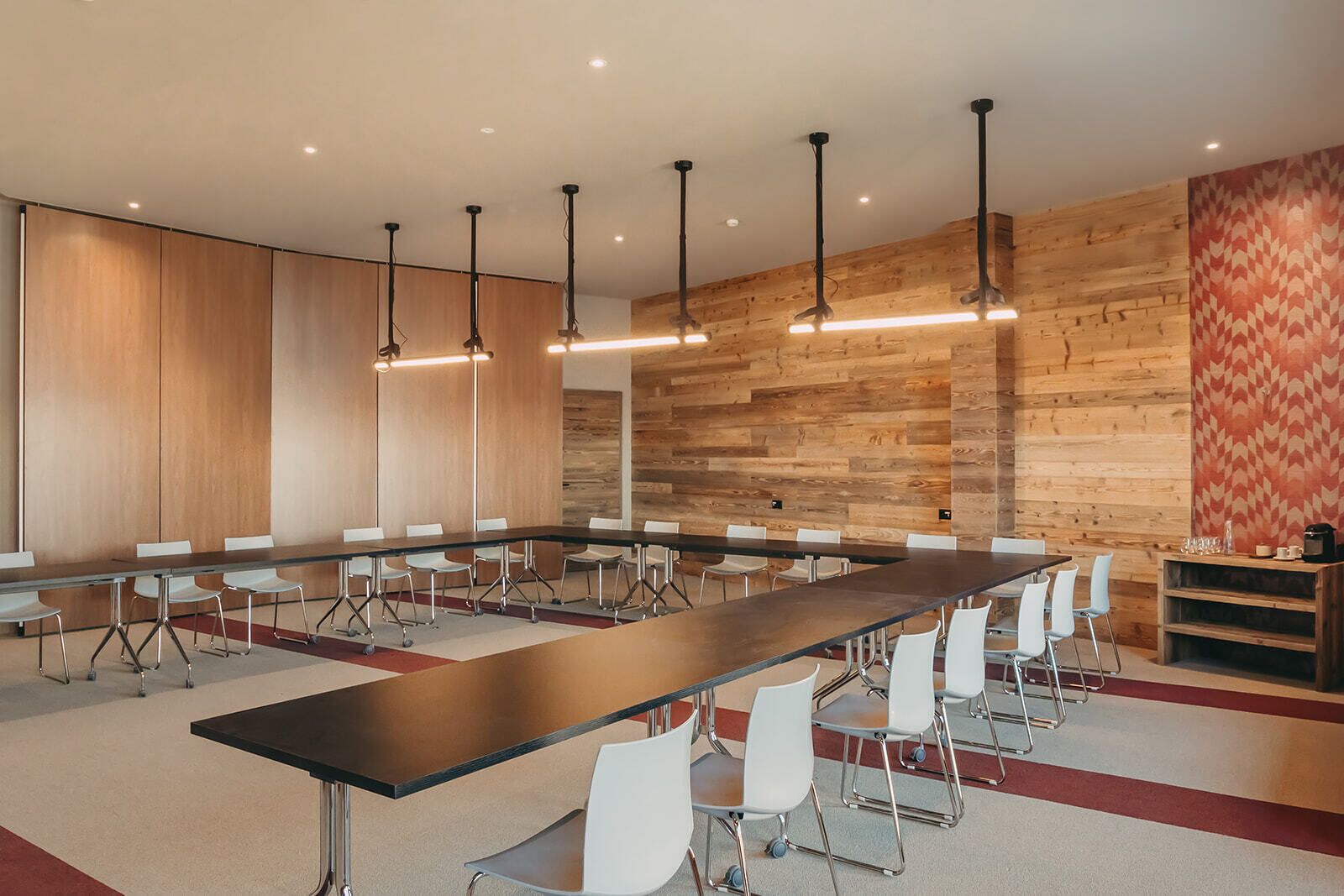 A conference room with a long table, white chairs, and wooden panel walls.