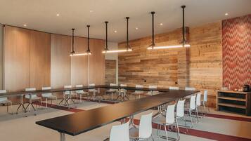 Una sala de conferencias con una larga mesa, sillas blancas y paneles de madera.