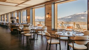 A restaurant with tables set for dining, large windows offering mountain views, and wooden interior design. - Eringer Hotel (Heremence)