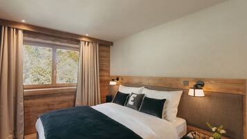 A bedroom with a large bed, wooden headboard, two bedside lamps, a nightstand, and a window with curtains.