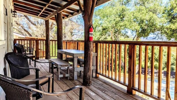 A covered outdoor area with wooden furniture, a fire extinguisher, and a view of trees and water. - # 6. The Hawks Hideout - Cabin W/ Lake Views (San Diego County)