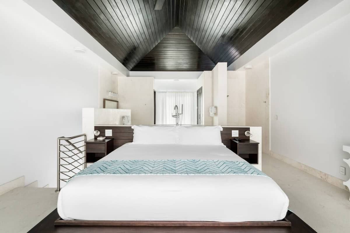 A modern hotel room with a large bed, wooden headboard, and a ceiling with exposed beams.