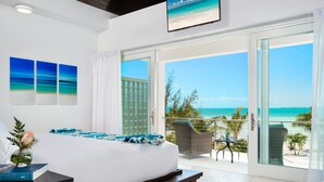 A hotel room with a bed, a bedside table, a TV, and a balcony with a view of the beach and ocean. - SulMare at Taylor Bay Luxury Villas (Providenciales)
