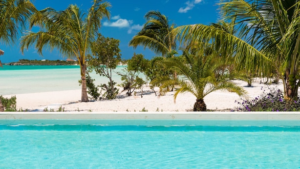 A pool area with clear blue water, surrounded by palm trees and a sandy beach. - SulMare at Taylor Bay Luxury Villas (Providenciales)