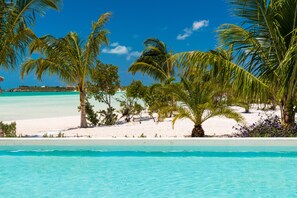 Une piscine à l’eau d’un bleu limpide, entourée de palmiers et bordée d’une plage de sable.