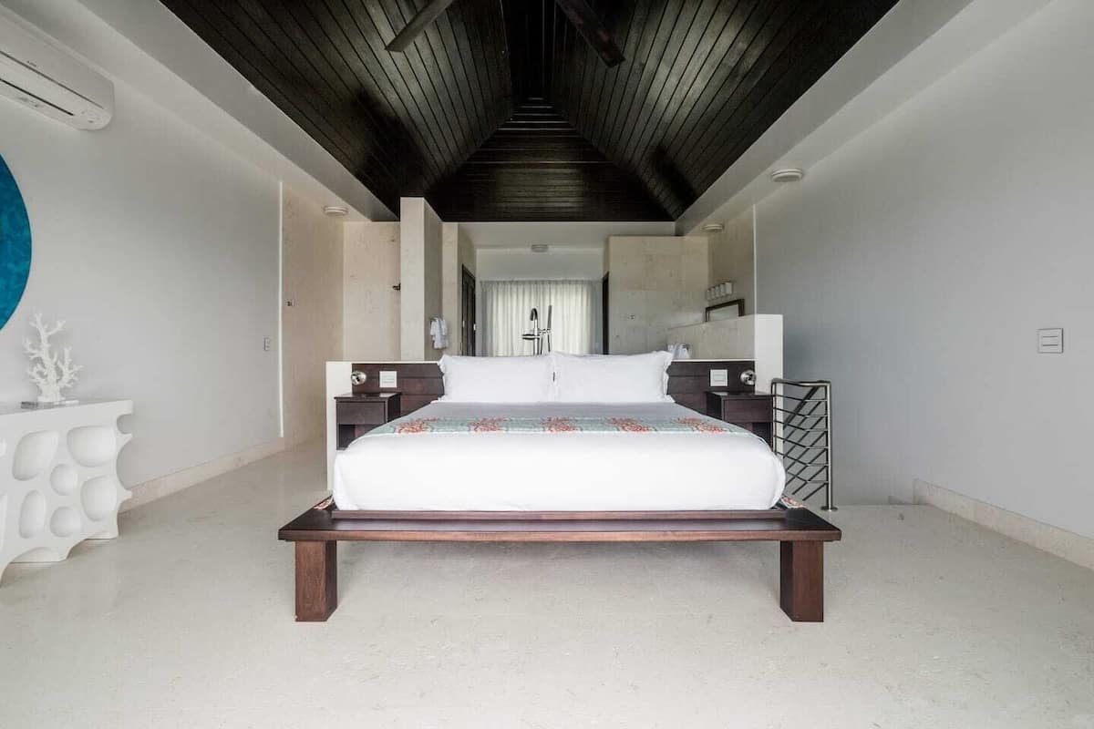 A spacious bedroom with a large bed, a wooden ceiling, and a white console table.